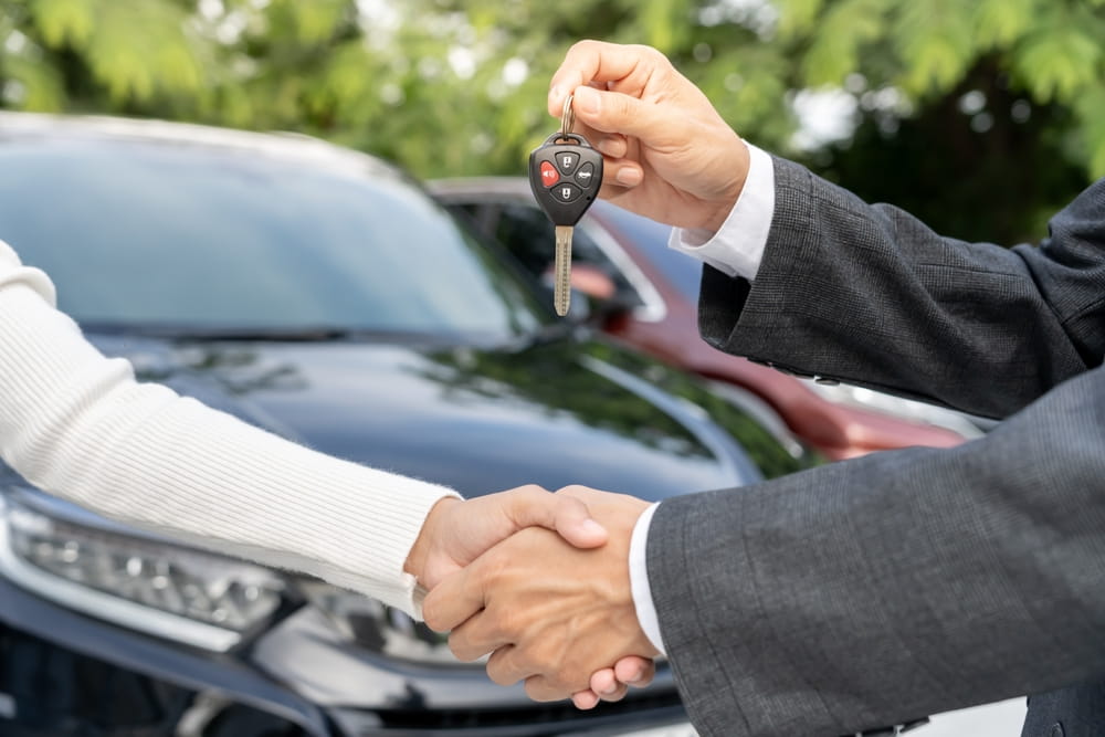 Rental agent handing car keys to a customer after a handshake
