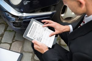 insurance adjuster Holding Digital Tablet Examining Damaged Car