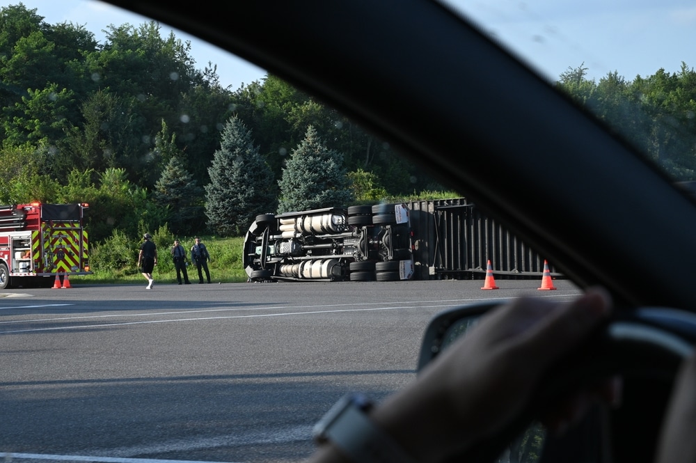 Truck rollover accident with trailer lying on its side near highway