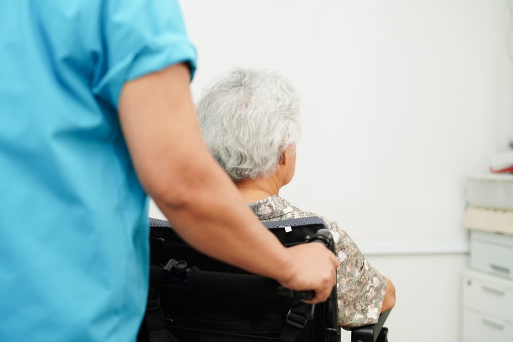 What Should I do if I Suspect Nursing Home Abuse in Oklahoma? 3 Caregiver pushing an older adult in a wheelchair down a hallway or medical room