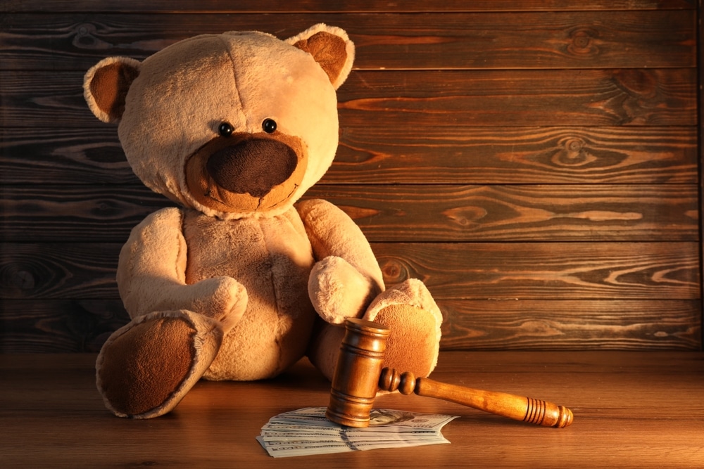 Oklahoma City Child Injury Lawyers 2 Teddy bear sitting beside a gavel and money on a wooden table