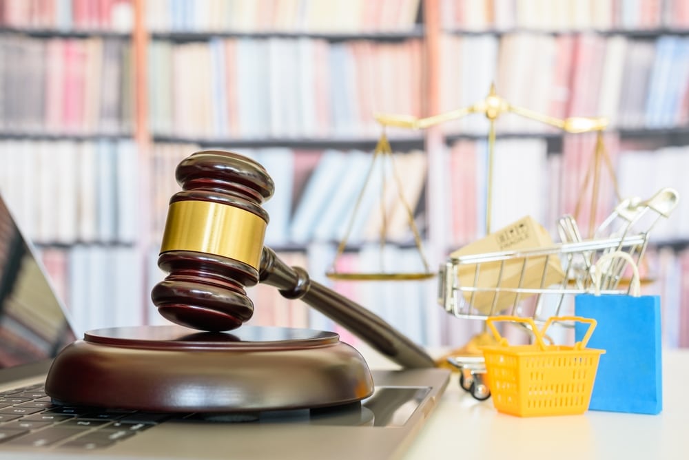 Gavel resting on a laptop with a miniature shopping cart and scales of justice in the background